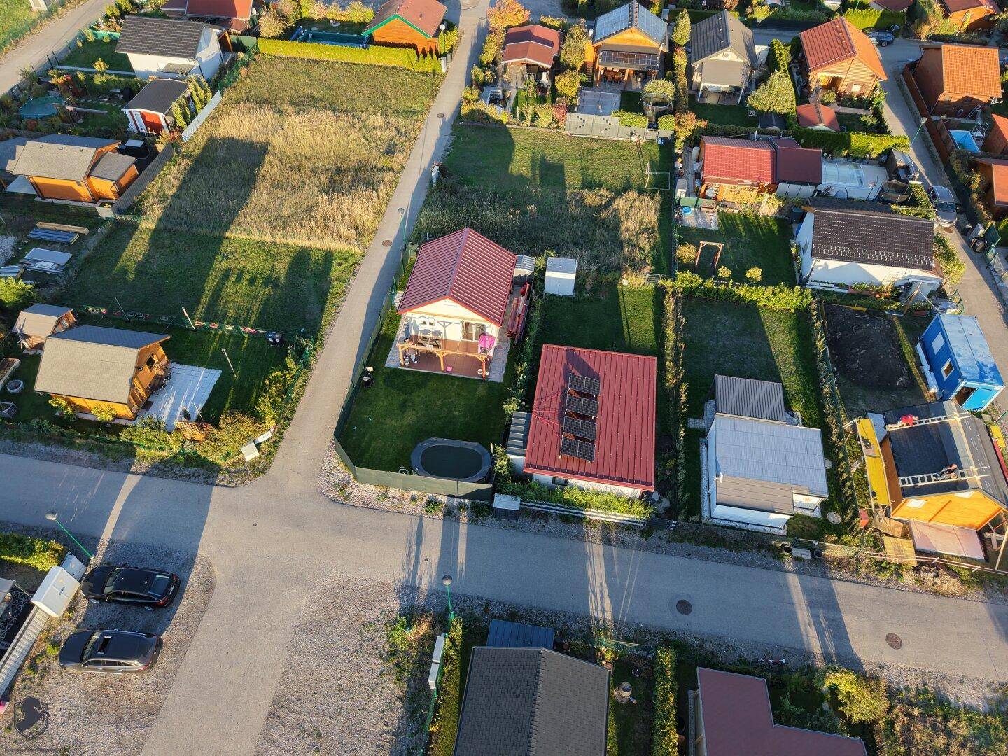 Luftaufnahme einer Siedlung mit mehreren Häusern, Gärten und einem Gebäude mit Solaranlage.