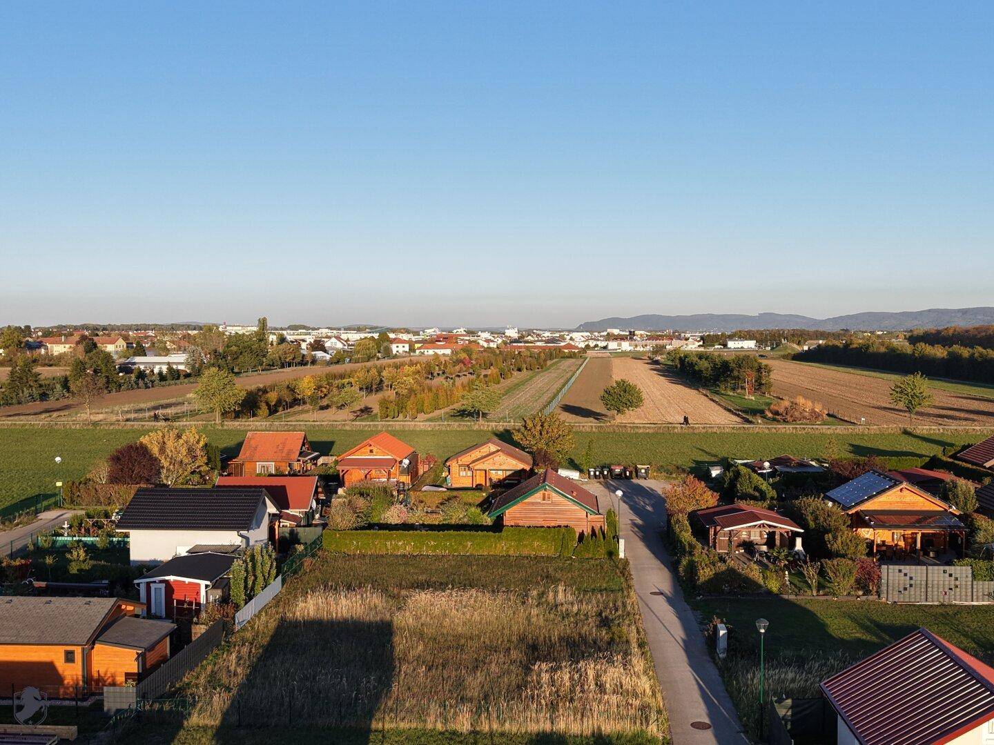 Panoramablick über eine ländliche Siedlung mit Feldern und Bergen im Hintergrund.