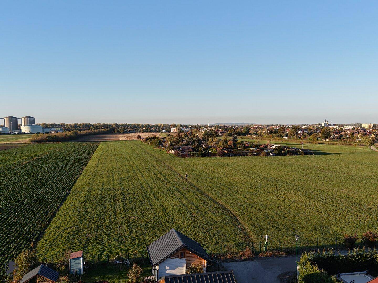 Blick über weite Felder mit Industrieanlagen und einer Stadt am Horizont.
