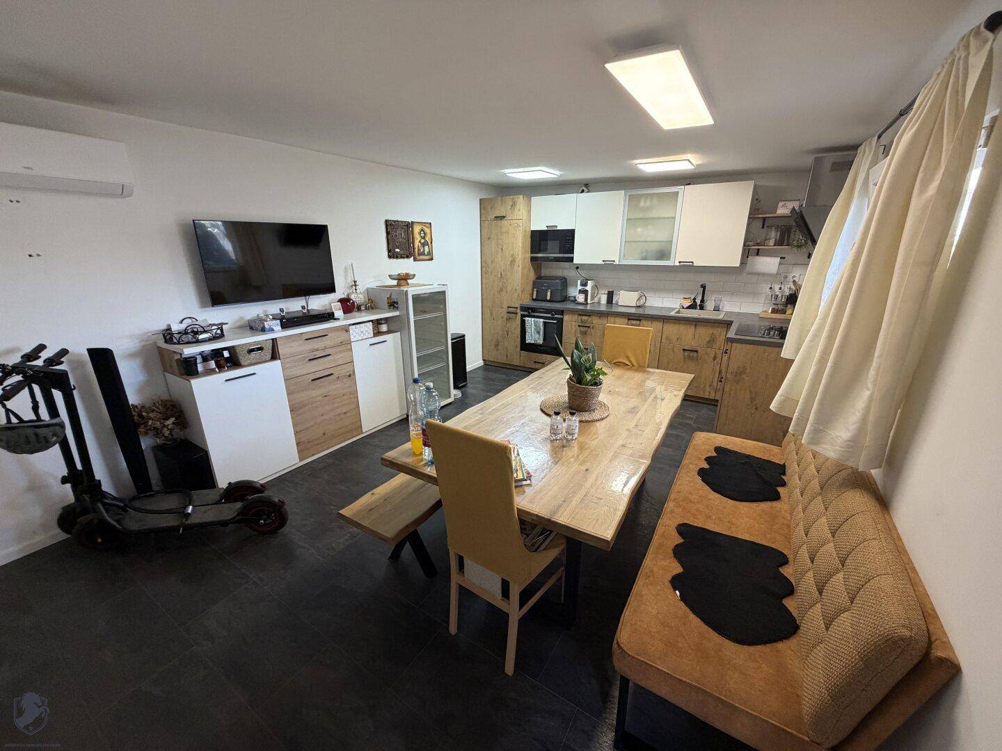 Offener Wohn- und Essbereich mit integrierter Küche, dunklem Fliesenboden und modernem Design.