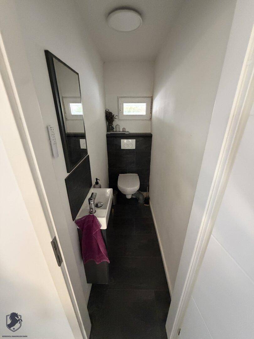Modernes Gäste-WC mit dunklen Fliesen, wandhängendem WC und kleinem Fenster.