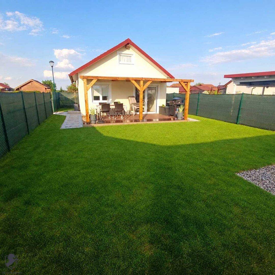 Gepflegter Garten mit Rasenfläche und einer möblierten Terrasse unter einer Holzpergola.