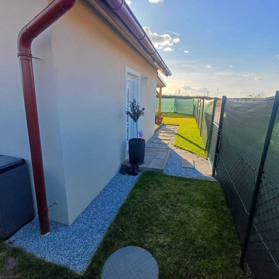 Schmaler Seitenweg entlang des Hauses mit Kies und kleiner Rasenfläche.