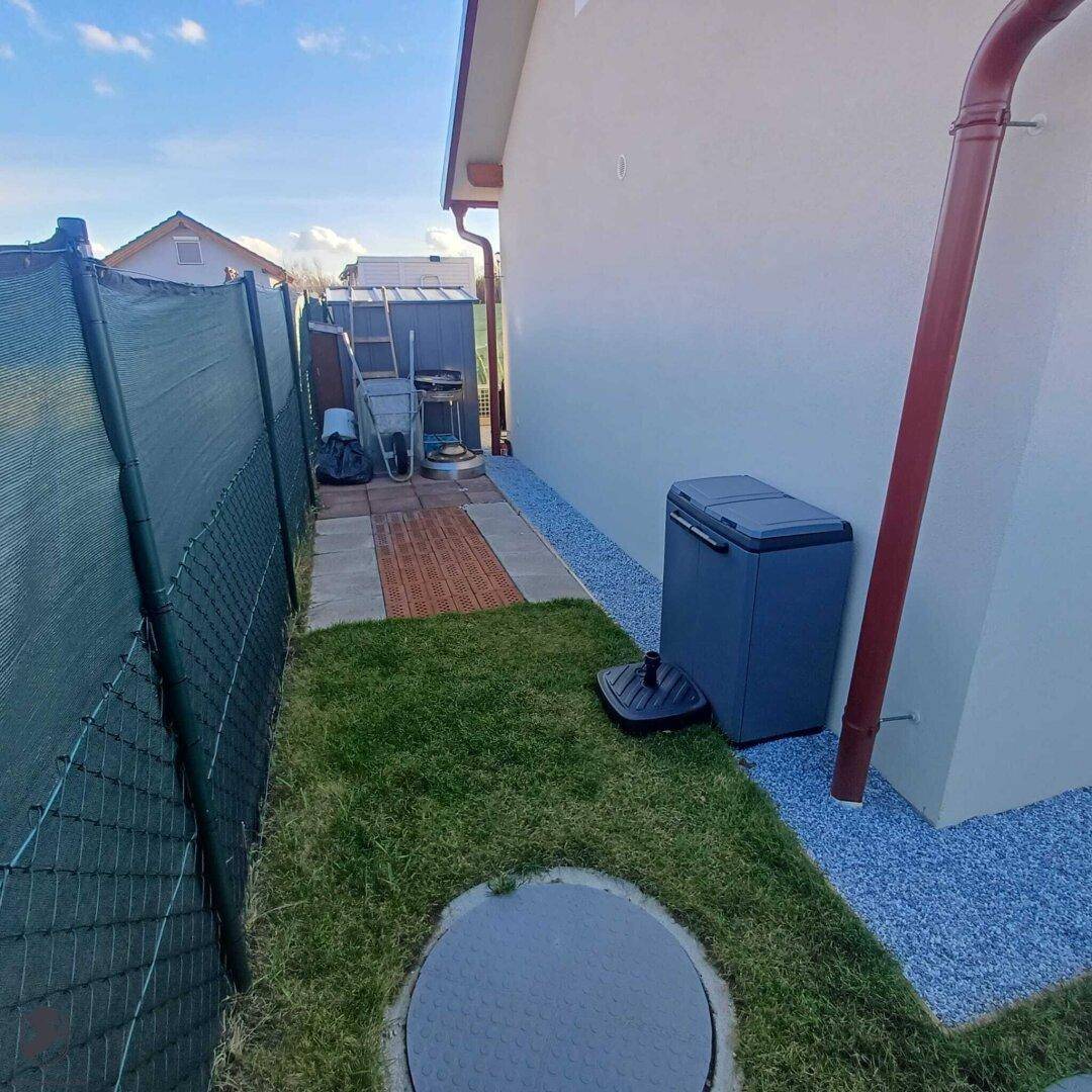 Seitenbereich des Hauses mit Rasen, Kiesweg und einem Gartenschuppen im Hintergrund.