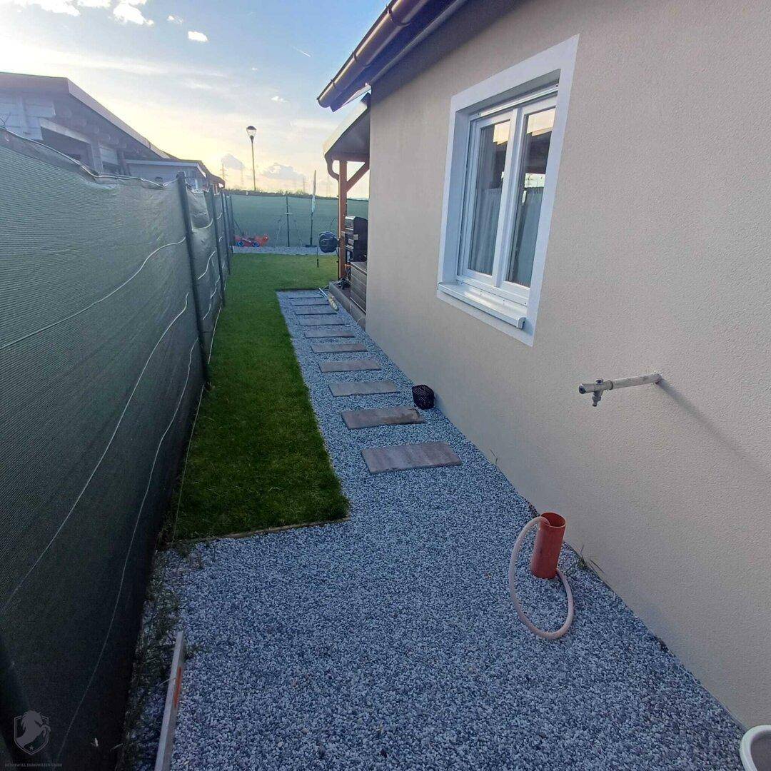 Seitenansicht des Hauses mit Fenster, Kiesweg und einem Wasseranschluss im Freien.