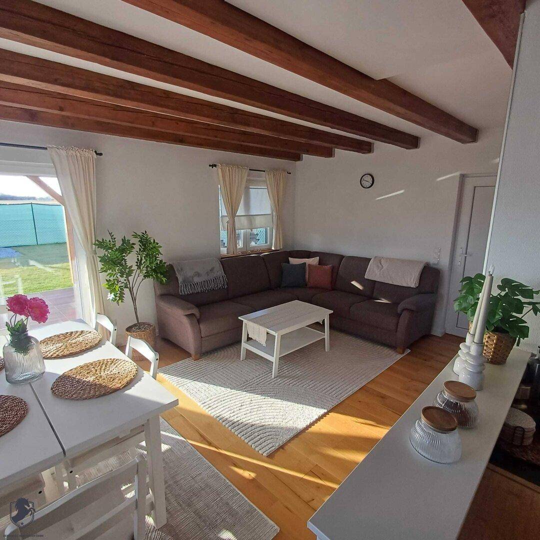 Helles Wohnzimmer mit Ecksofa, Holzbalken und Zugang zur Terrasse oder Garten.