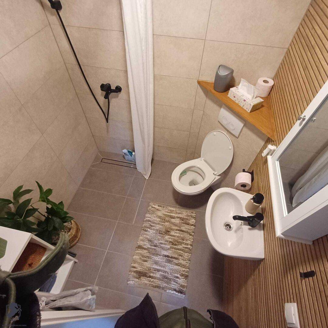 Modernes Badezimmer mit begehbarer Dusche, WC, Waschbecken und Holzwandverkleidung.