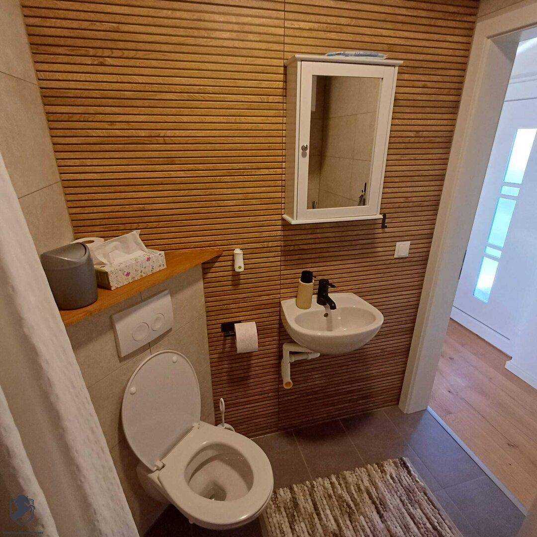Helles Badezimmer mit WC, Waschbecken, Spiegelschrank und dekorativer Holzwand.