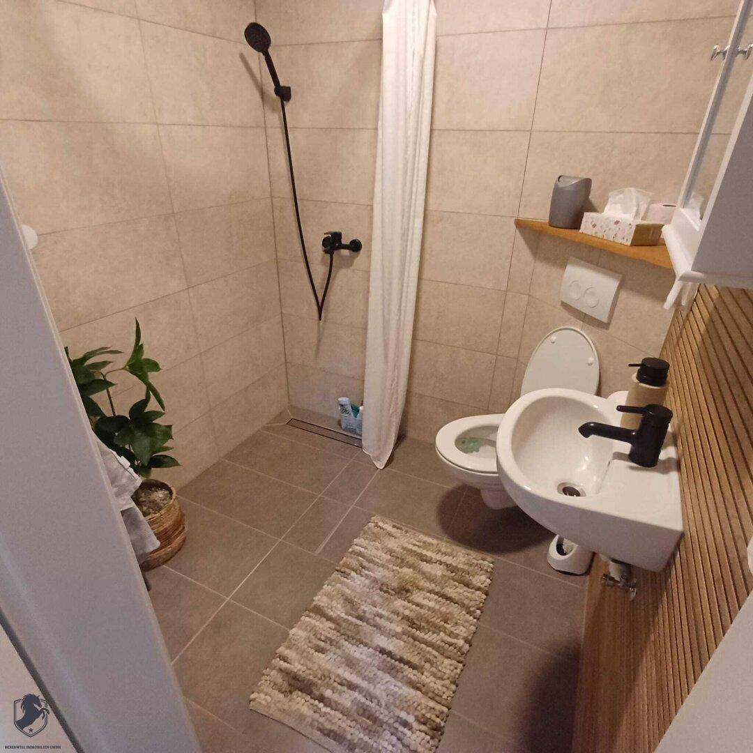 Funktionales Badezimmer mit Duschbereich, WC, kleinem Waschbecken und Holzdetails.