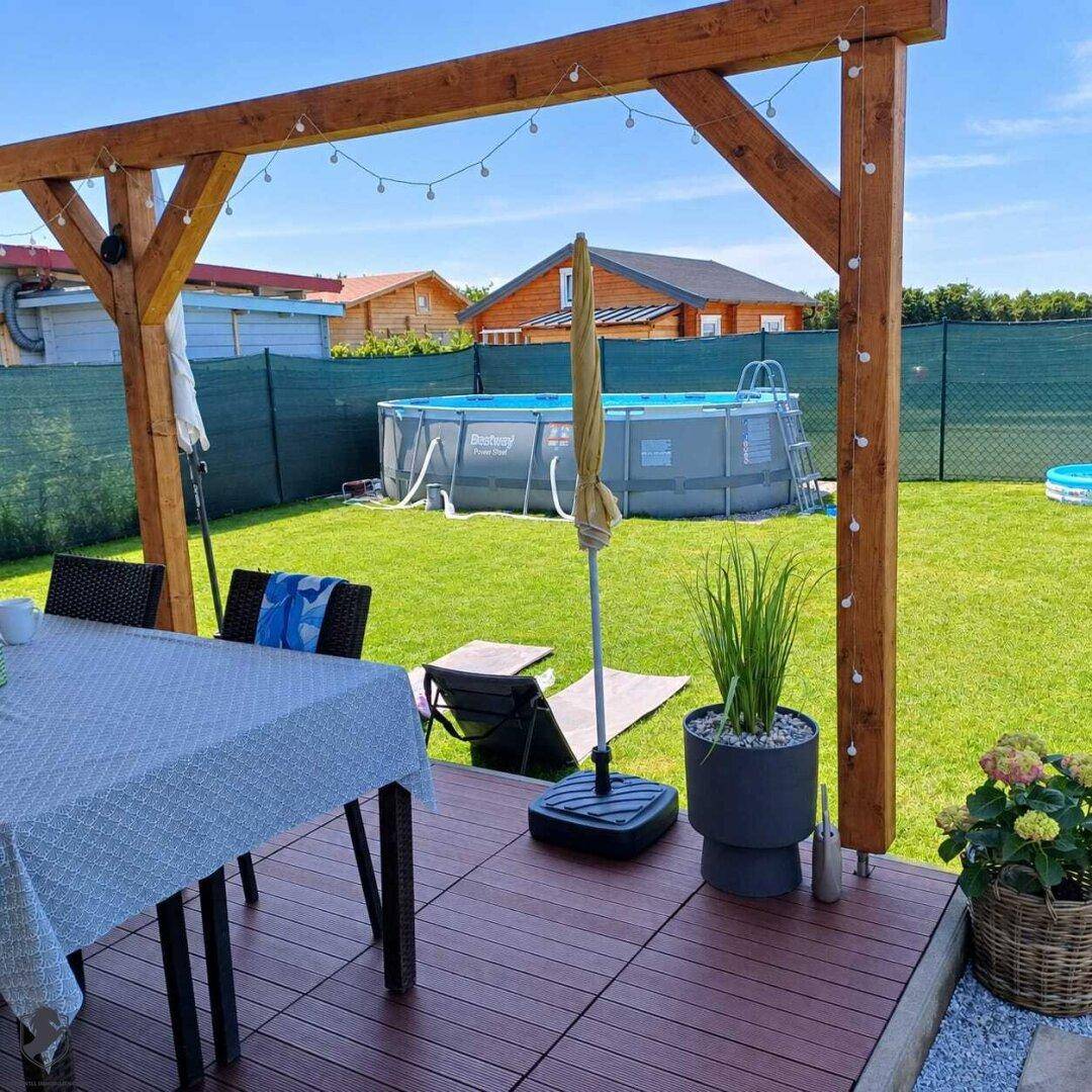 Sonniger Gartenbereich mit Holzpergola, Terrasse, Rasenfläche und einem Aufstellpool.
