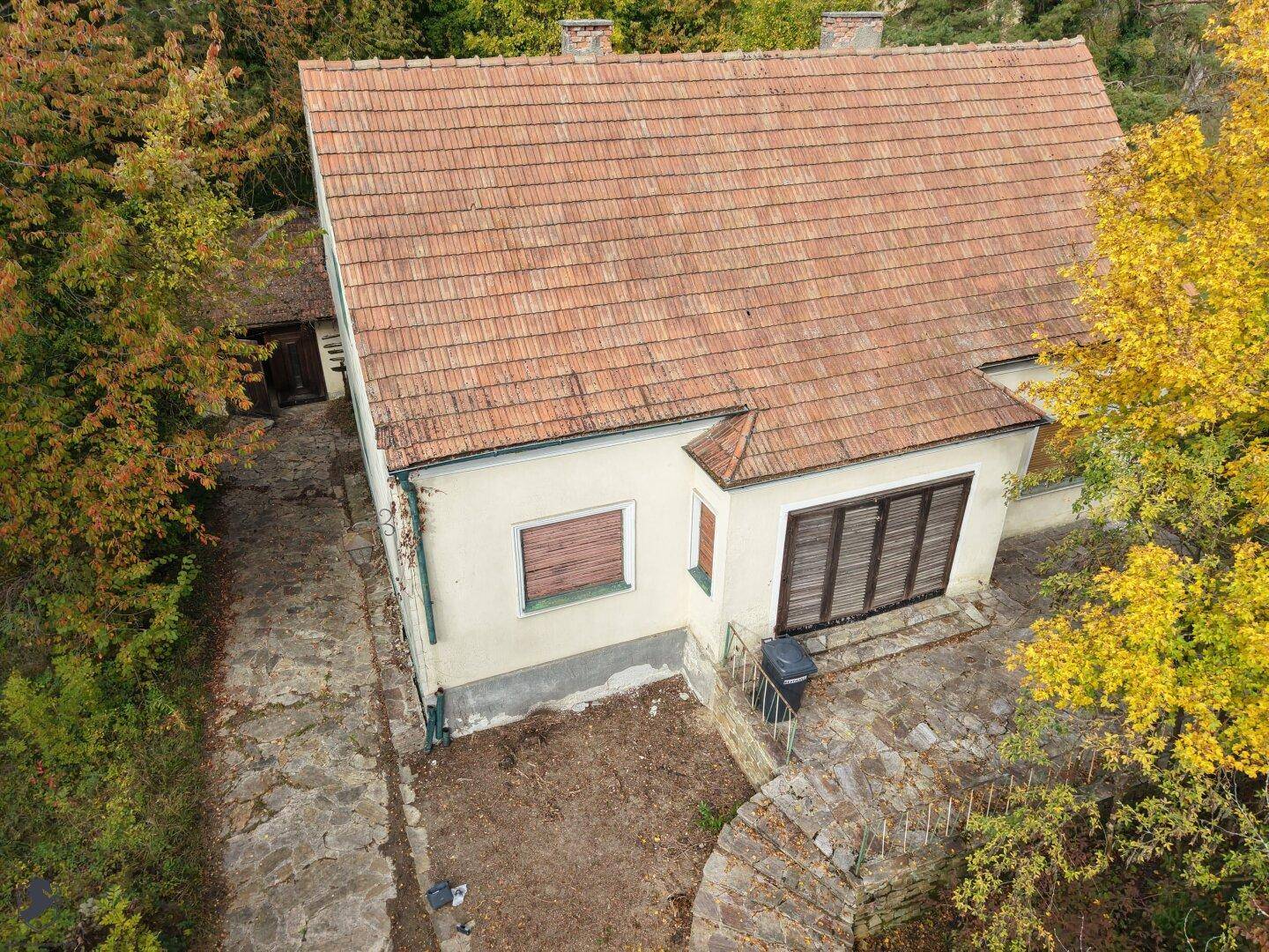 Rückansicht des Hauses von oben mit Ziegeldach, kleiner Terrasse und einem Nebengebäude.