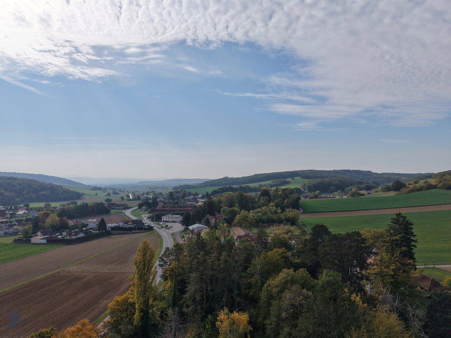 Panoramablick über die weite Landschaft mit Feldern, Wäldern und einem kleinen Dorf in der Ferne.