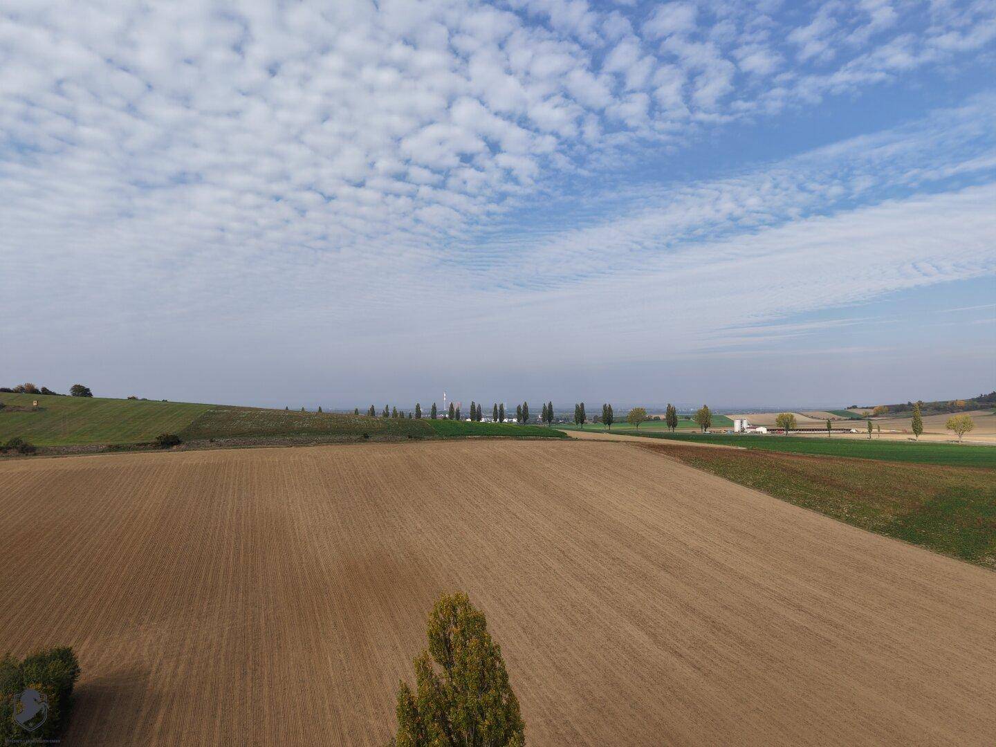 Luftaufnahme von weiten, frisch gepflügten Feldern unter einem bewölkten Himmel.