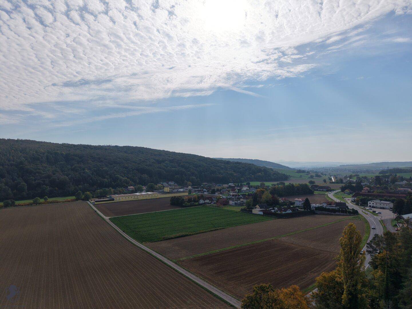 Luftaufnahme eines Dorfes eingebettet in eine Landschaft aus Feldern und bewaldeten Hügeln.