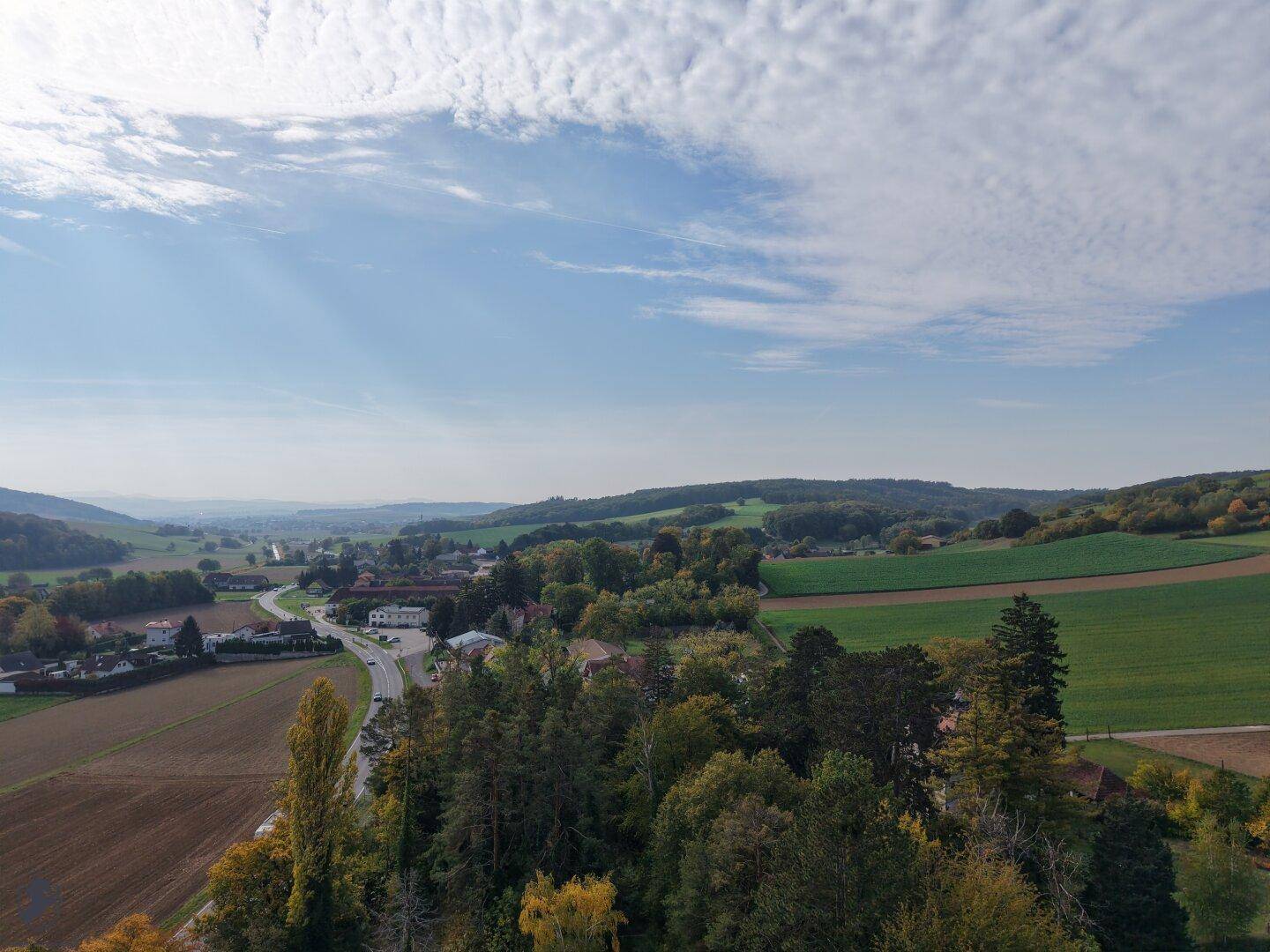 Panoramablick auf ein ländliches Dorf, umgeben von weiten Feldern und grünen Wäldern.