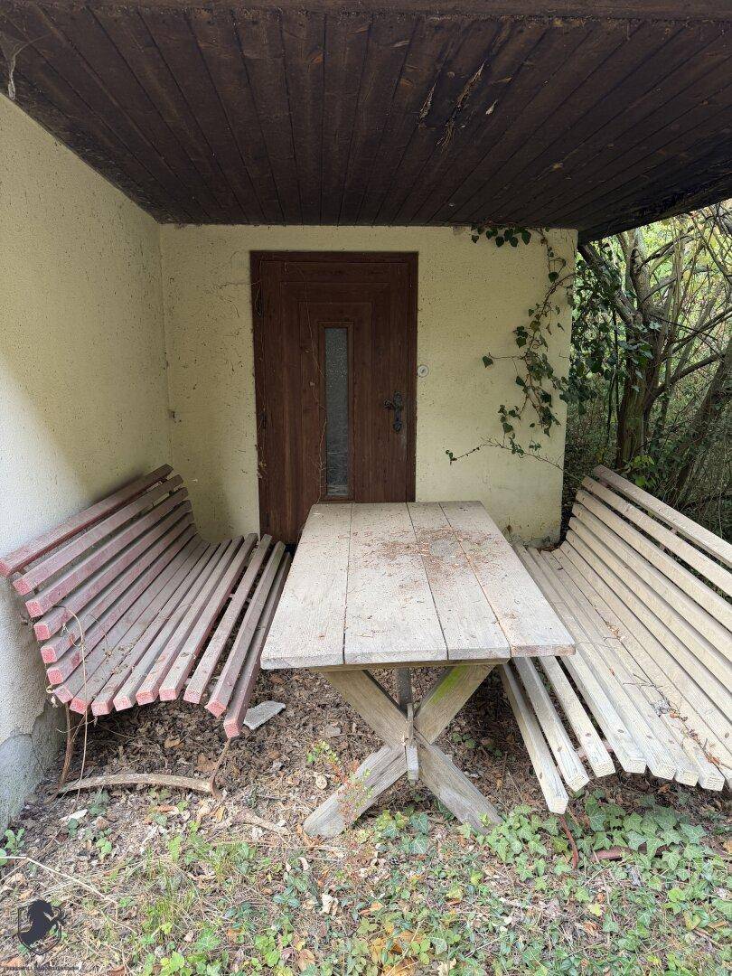 Überdachter Außenbereich mit rustikalem Holztisch und Bänken, ideal für Mahlzeiten im Freien.
