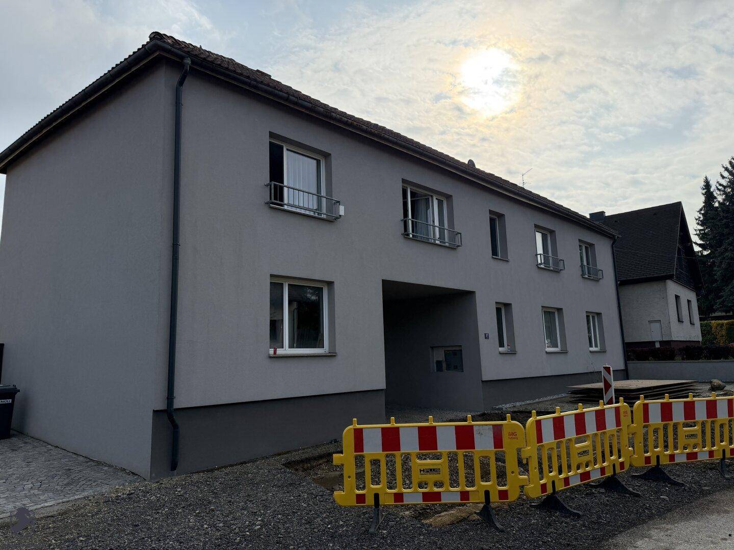 Seitenansicht des renovierten Gebäudes mit Durchfahrt und Bauabsperrungen unter sonnigem Himmel.