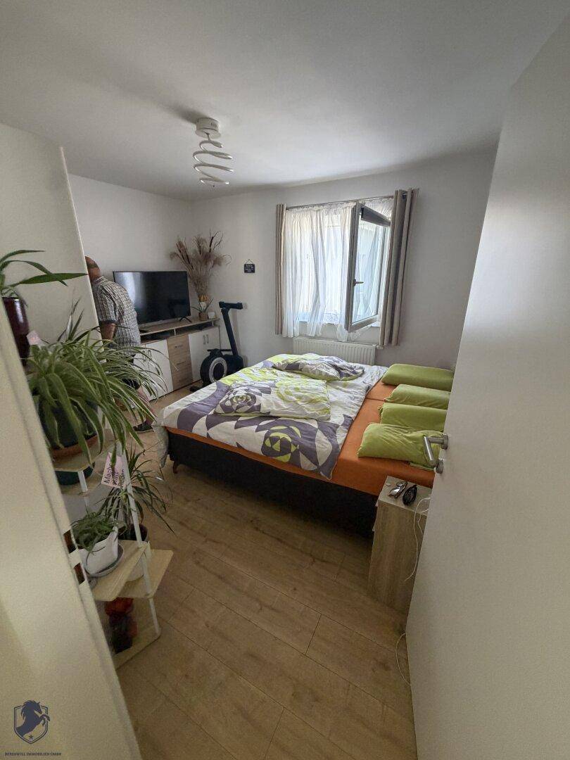 Schlafzimmer mit Laminatboden, Doppelbett und Fenster, das viel Tageslicht hereinlässt.