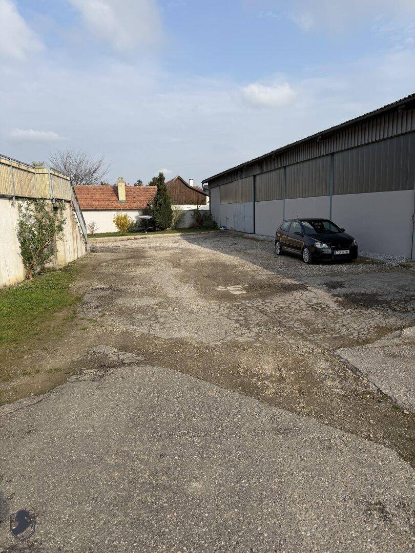 Weitläufiger, unbefestigter Außenbereich neben einer großen Halle, ideal für Parkplätze oder Lagerung.
