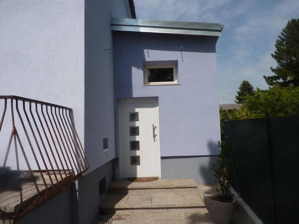 Eingangsbereich des Hauses mit weißer Tür, Steinstufen und kleiner Überdachung.