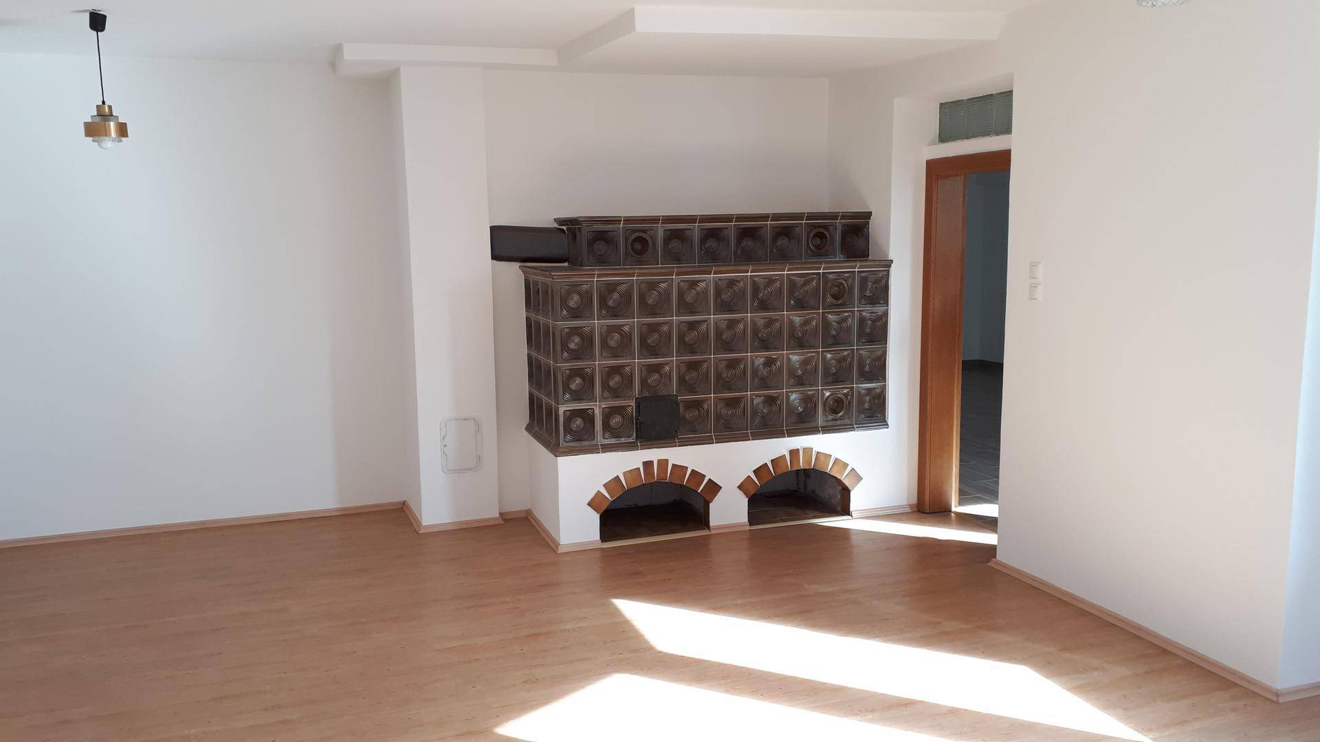 Heller Wohnraum mit hellem Laminatboden und einem traditionellen Kachelofen als Blickfang.