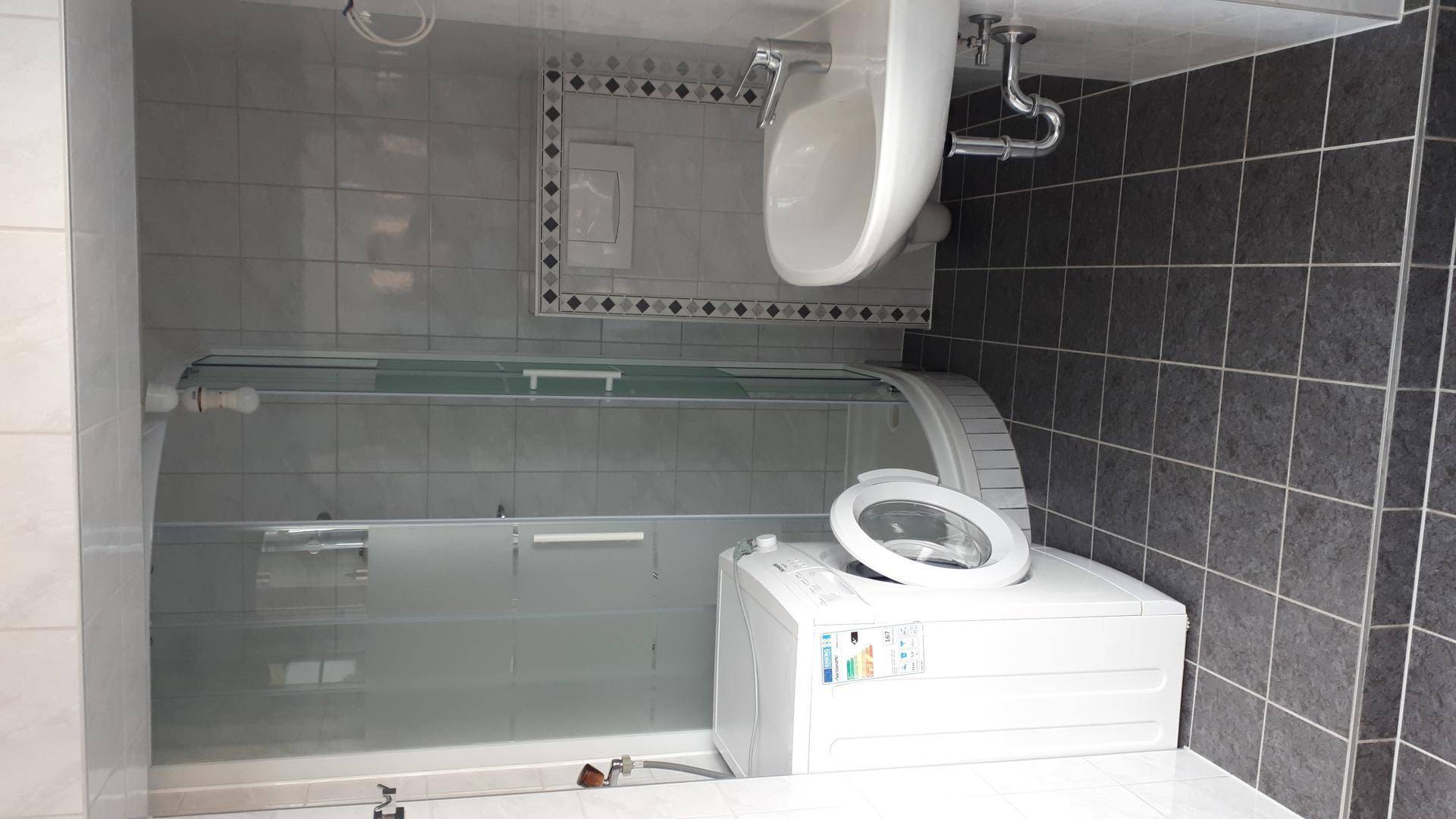 Modern gefliestes Badezimmer mit Waschbecken, Duschkabine und integrierter Waschmaschine.
