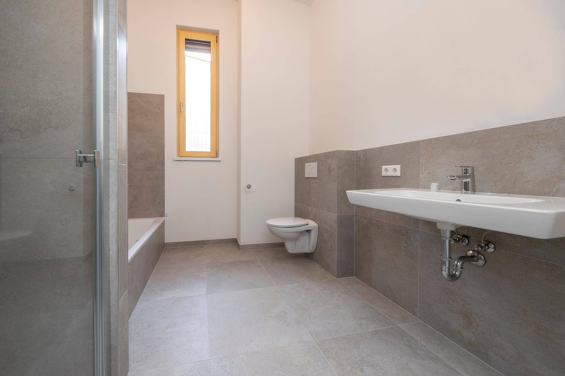 Modernes Badezimmer mit WC, Waschbecken, Fliesen und Fenster.