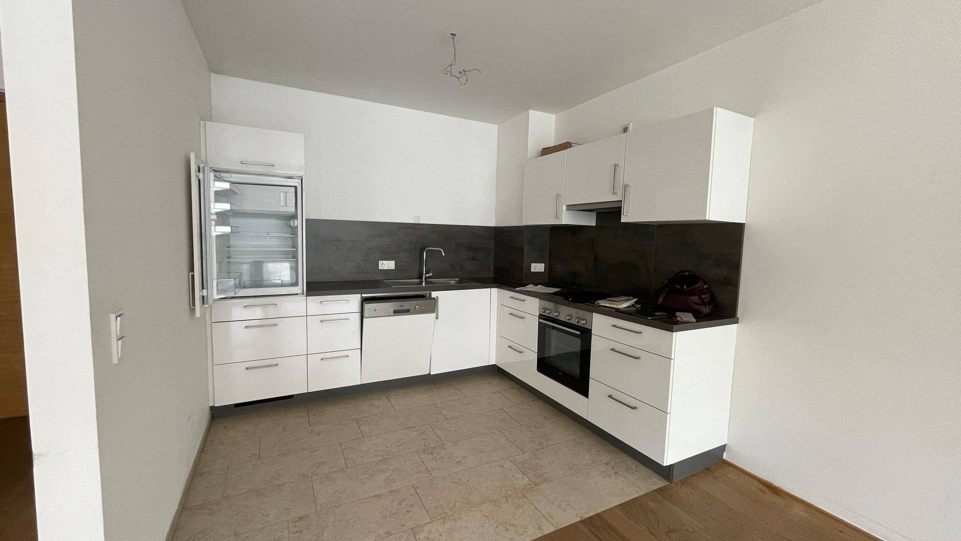 Moderne Einbauküche mit weißen Schränken, dunkler Arbeitsplatte und integrierten Geräten.