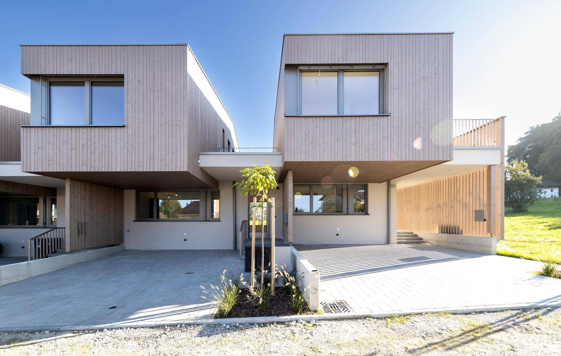 Vorderansicht moderner Häuser mit Holzfassade und gepflasterter Zufahrt.