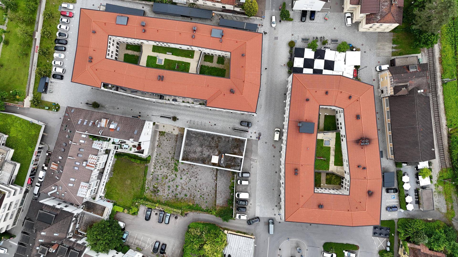 Draufsicht auf zwei U-förmige Gebäude mit roten Dächern und begrünten Innenhöfen, umgeben von städtischer Infrastruktur und Parkplätzen.