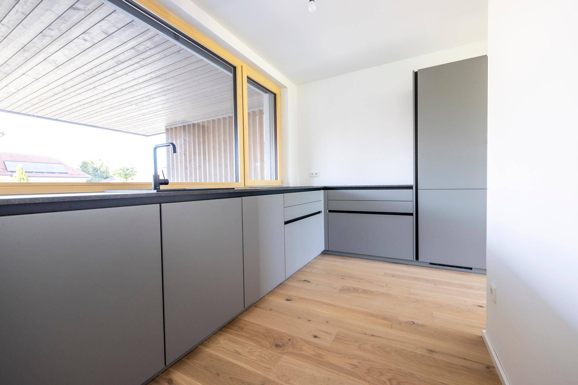 Funktionale Küche mit grauen Schränken, integriertem Backofen und Holzboden.
