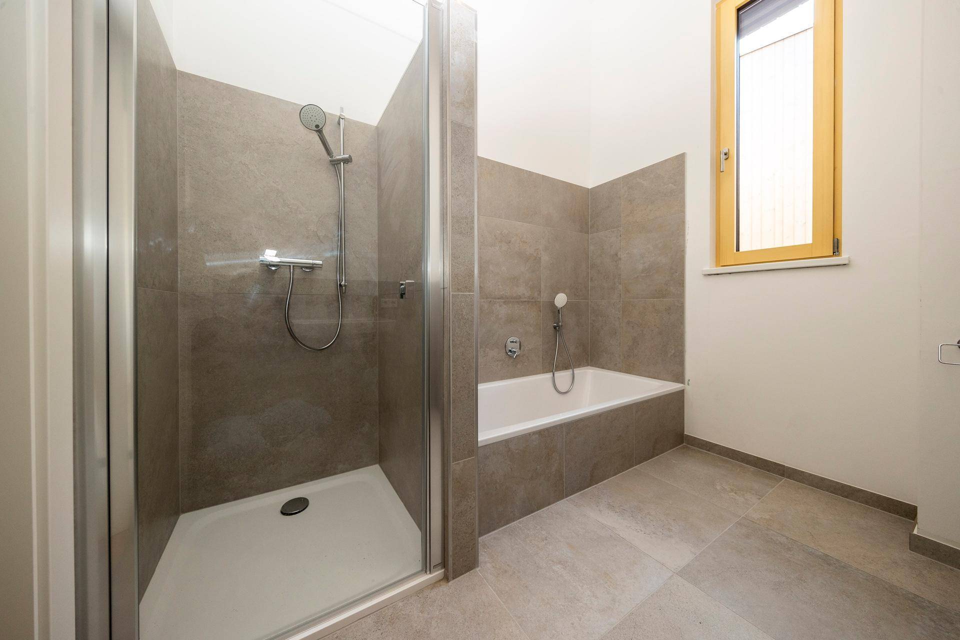Helles Badezimmer mit Badewanne, Dusche, Fliesen und Fenster.