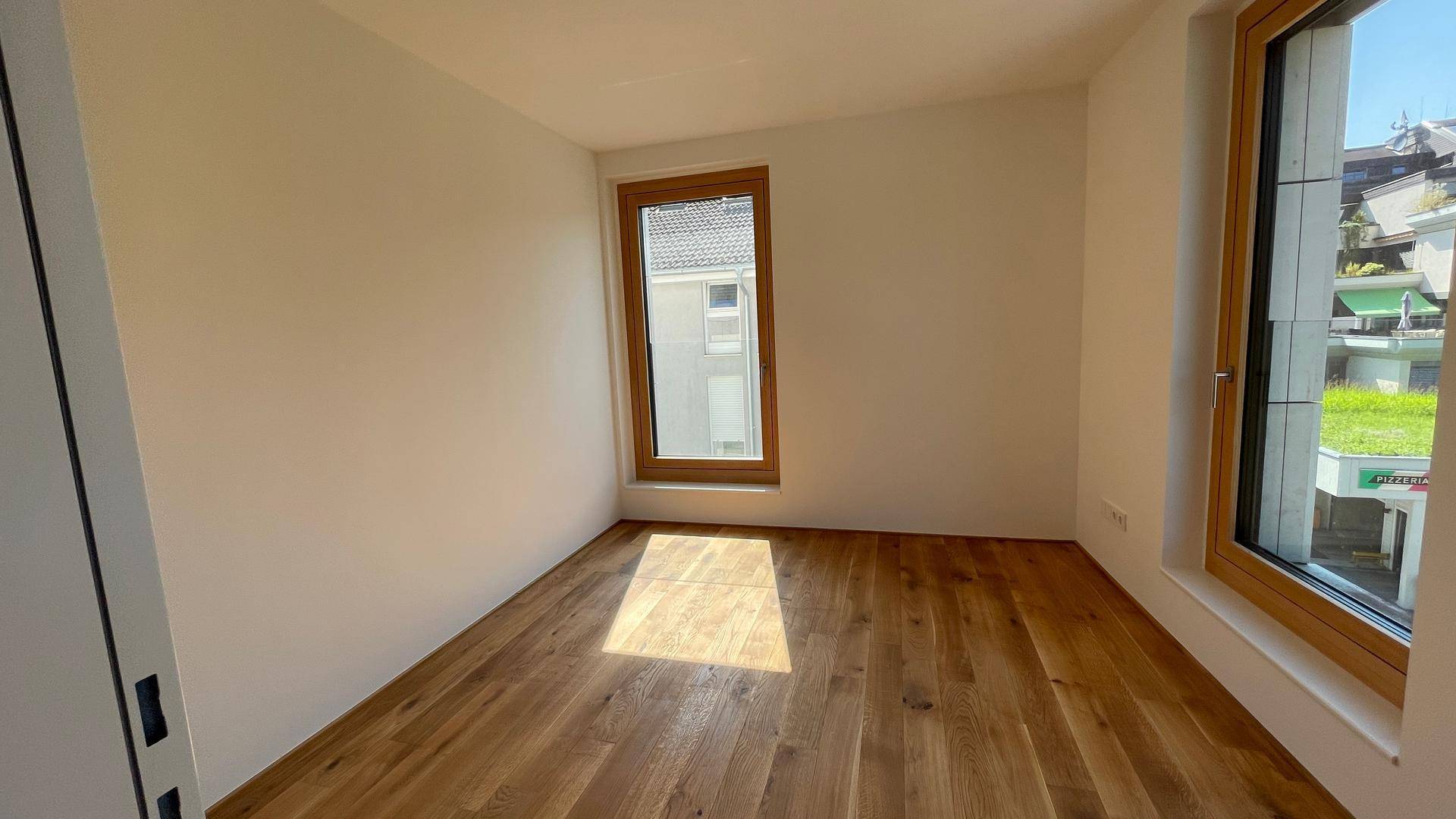 Weiteres Schlafzimmer mit Holzboden und zwei Fenstern, die den Raum gut belichten.