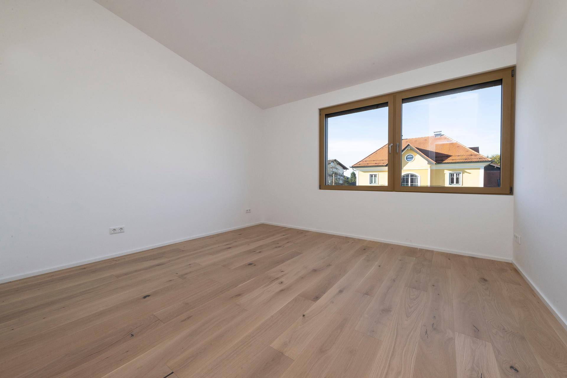 Schlafzimmer mit Holzboden und Fenster mit Blick auf ein Nachbarhaus.