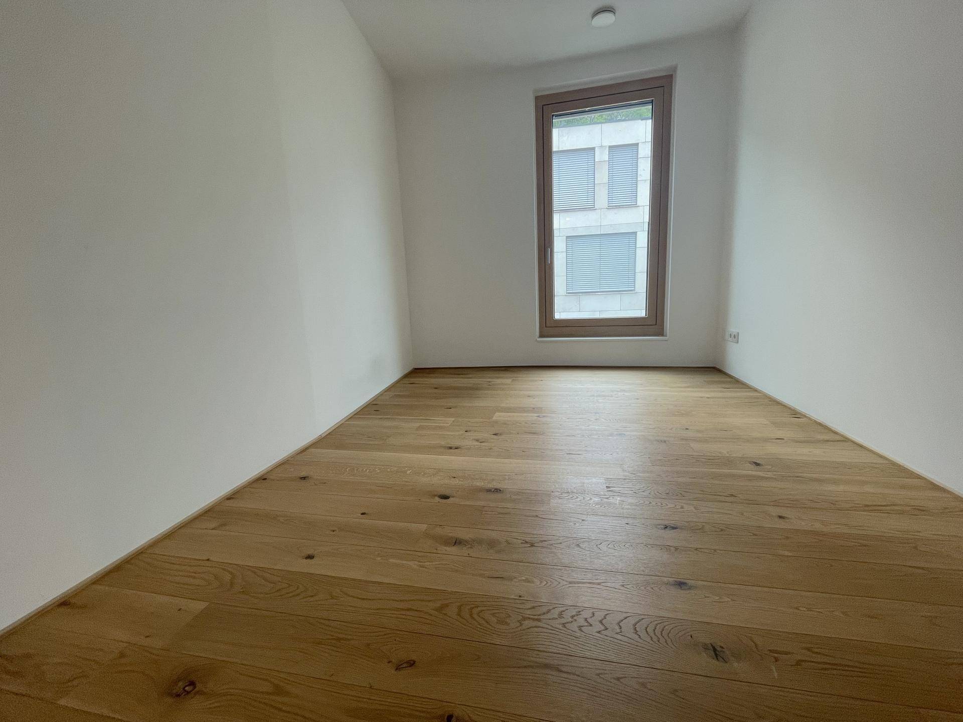 Kleiner, heller Raum mit Holzboden und einem Fenster, ideal als Schlaf- oder Arbeitszimmer.