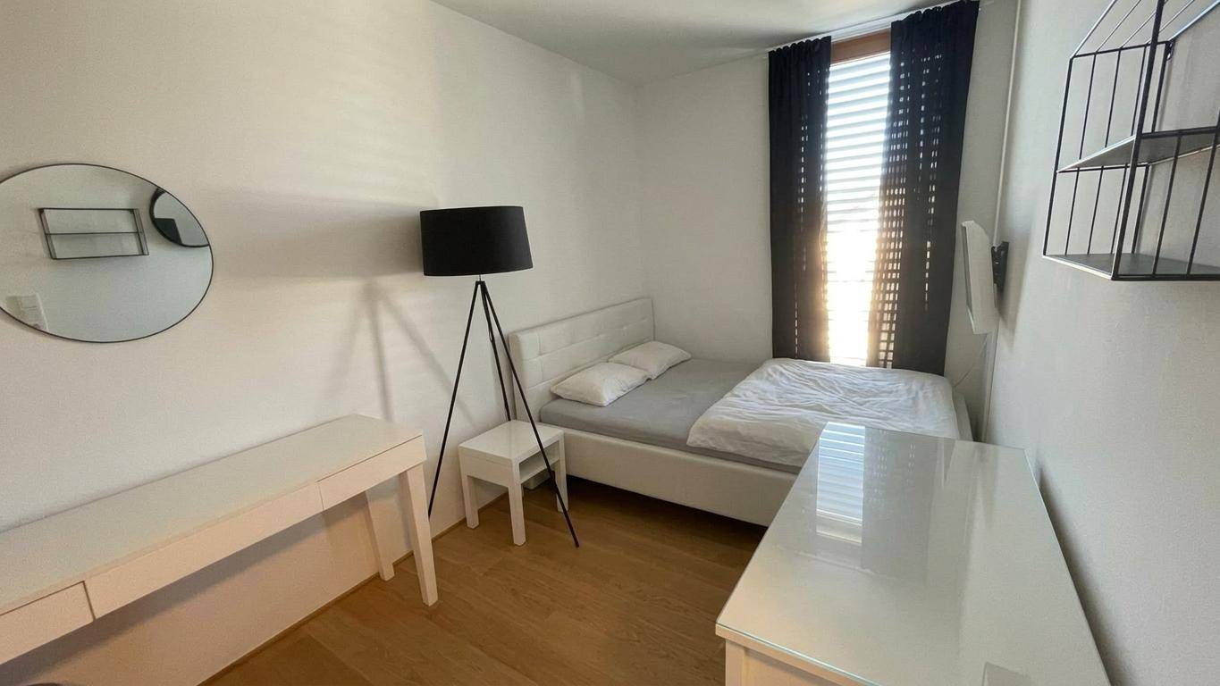 Modern eingerichtetes Schlafzimmer mit Einzelbett, Schreibtisch und dunklen Vorhängen.