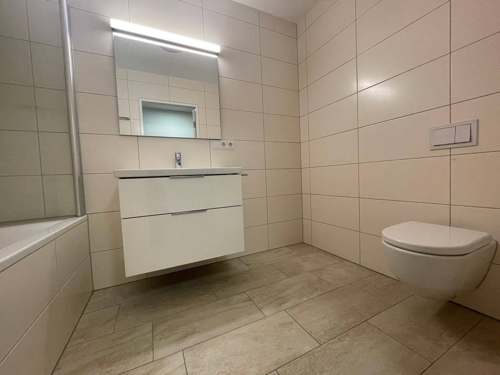 Modernes Badezimmer mit hellen Fliesen, schwebendem Waschtisch, Badewanne und Wand-WC.