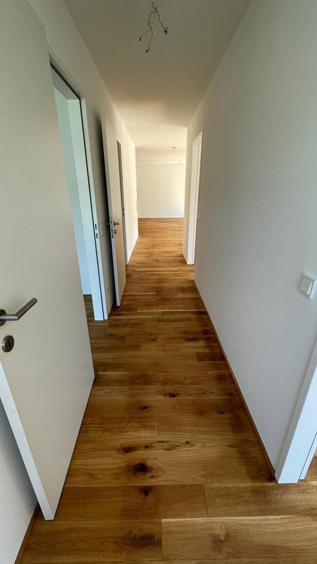 Langer Flur mit Holzboden, der zu verschiedenen Räumen der Wohnung führt.