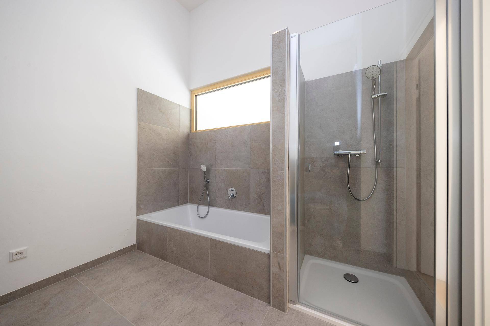 Modernes Badezimmer mit Badewanne, Dusche und Fliesenboden.