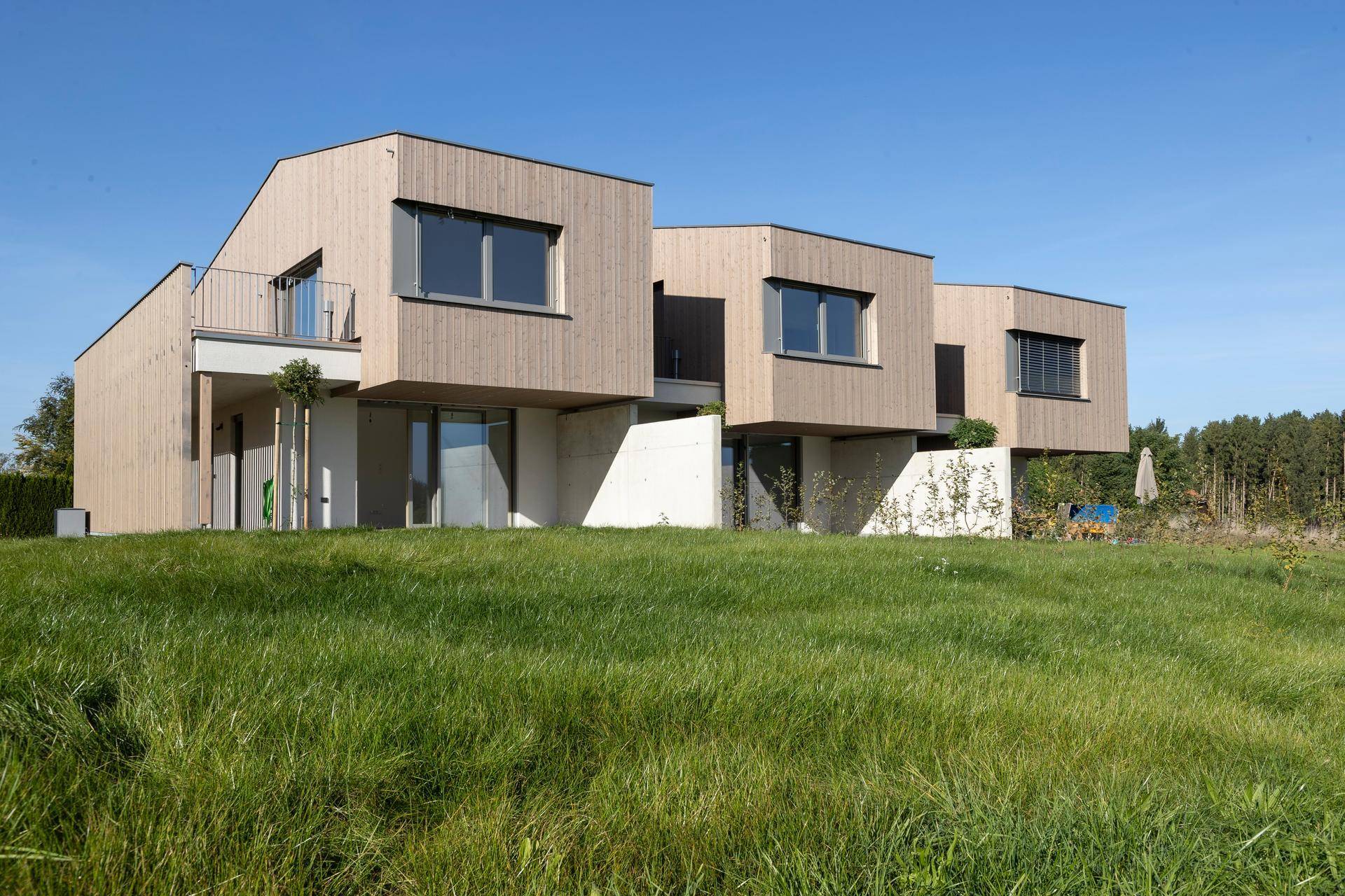Moderne Reihenhäuser mit Holzfassade und weitem Blick ins Grüne.