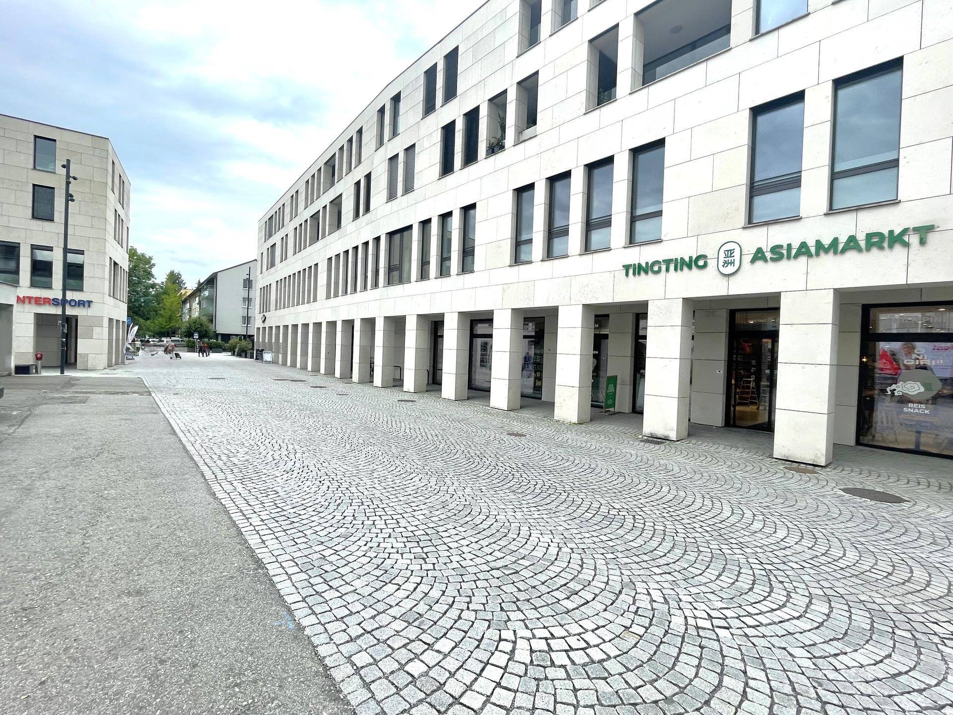 Moderne Gebäudefassade mit Geschäften im Erdgeschoss und gepflastertem Fußgängerbereich.