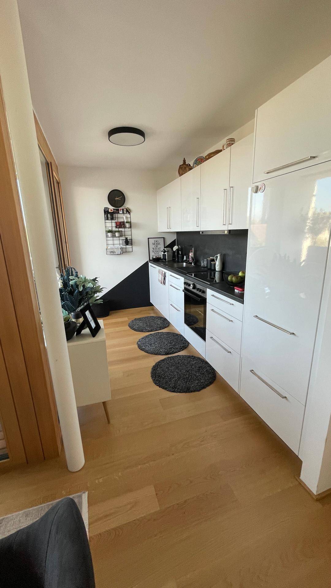 Moderne weiße Küche mit Hochglanzfronten, dunkler Arbeitsplatte und Holzboden.
