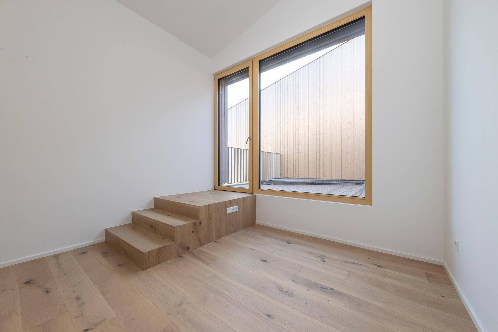 Helles Schlafzimmer mit Holzboden und Fenster mit integrierten Stufen.