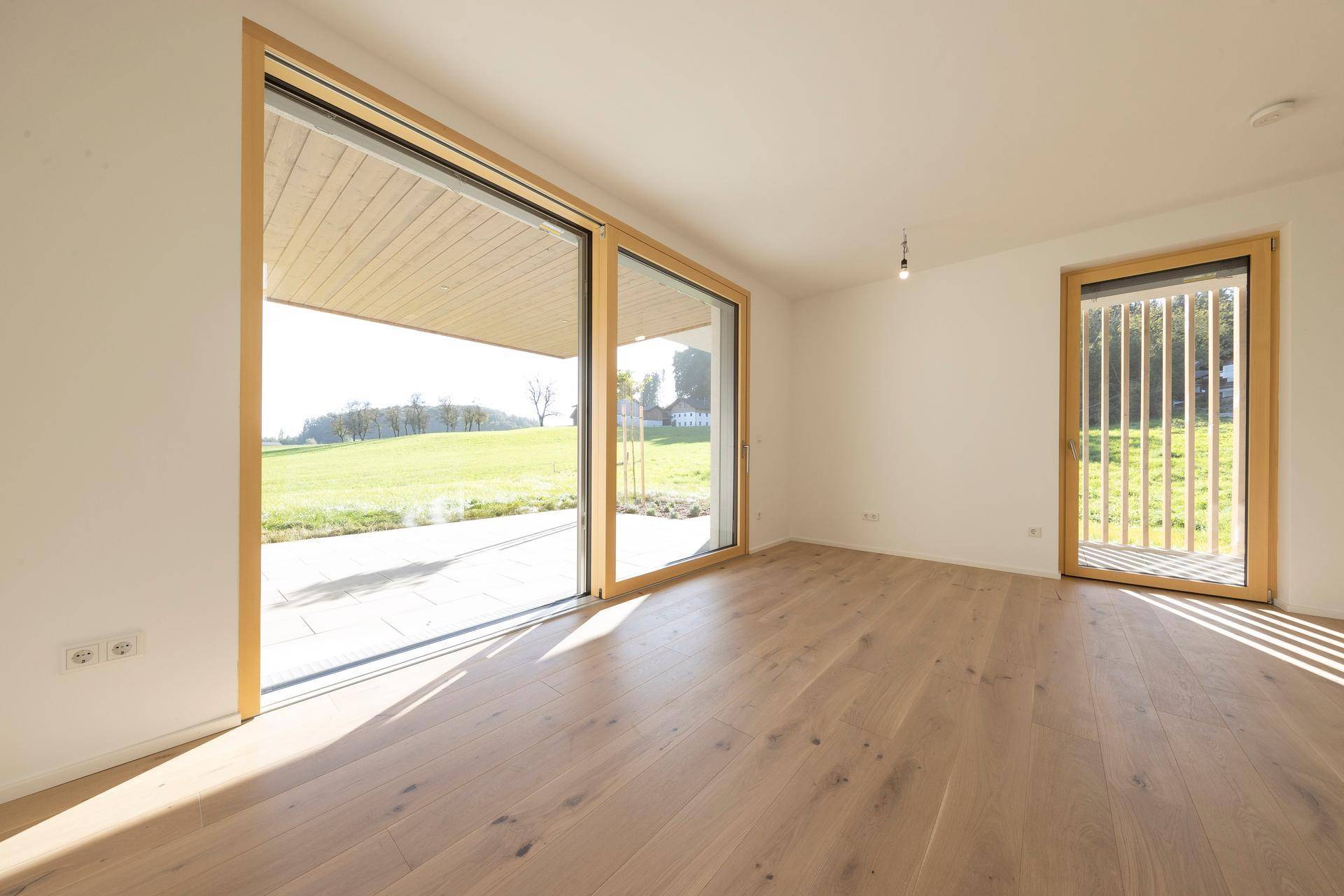 Lichtdurchfluteter Wohnbereich mit Holzboden und großen Schiebetüren zum Garten.