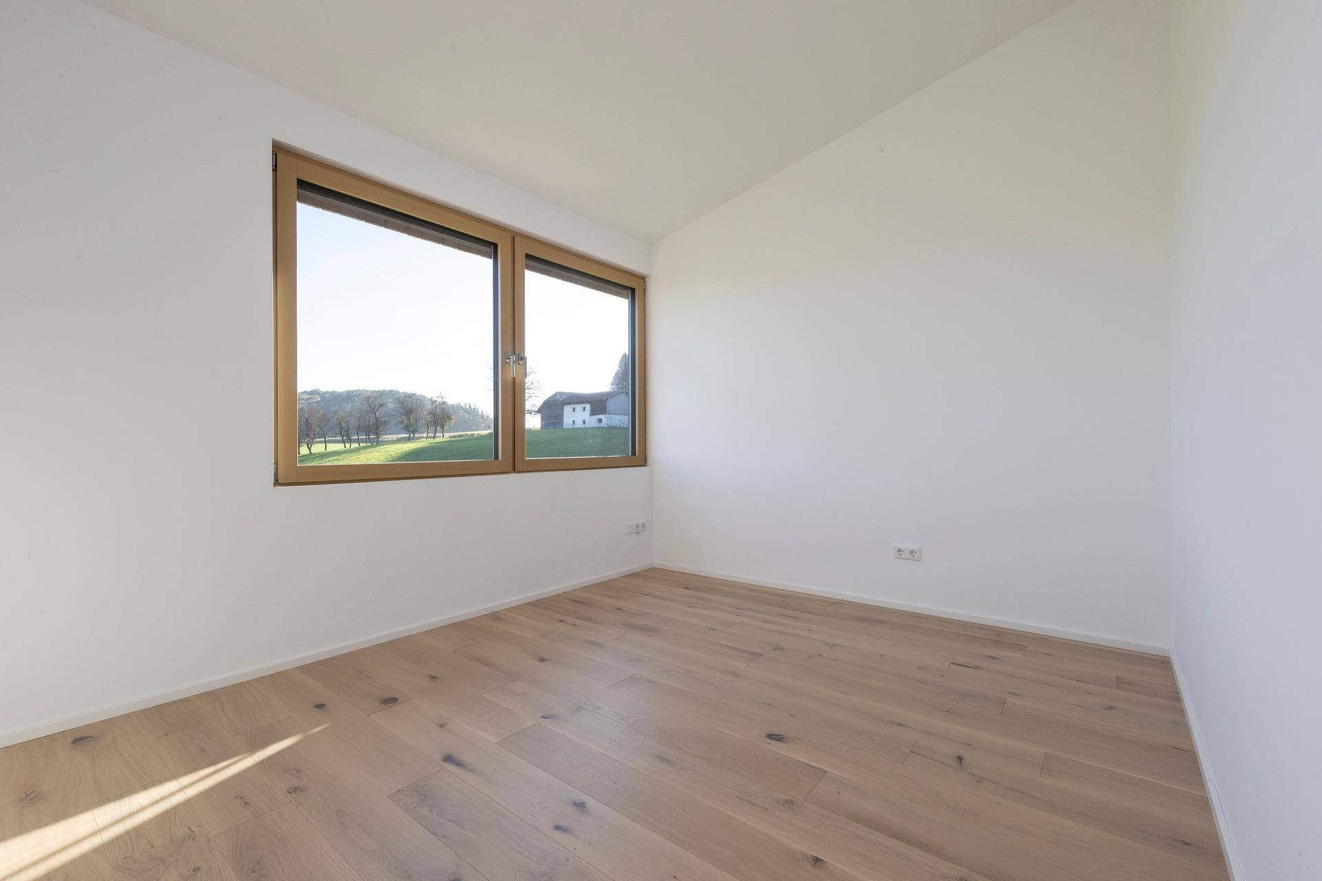 Schlafzimmer mit Holzboden und Fenster mit Blick ins Grüne.