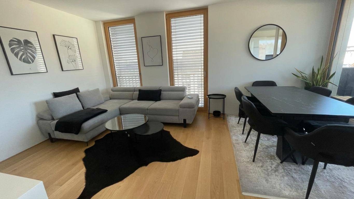 Offener Wohn- und Essbereich mit grauem Sofa, schwarzem Esstisch und Holzboden.