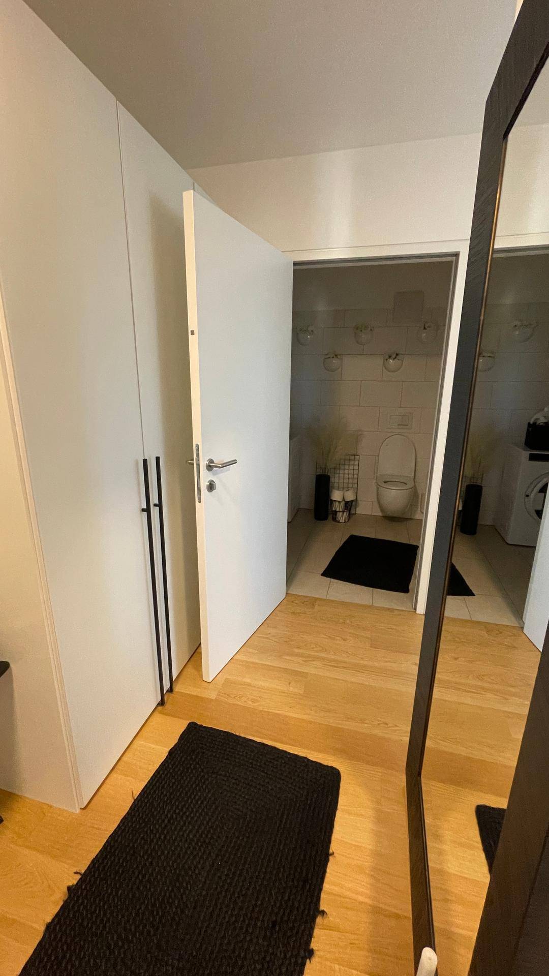 Heller Flur mit Holzfußboden, Einbauschränken und Blick in ein Badezimmer mit WC.