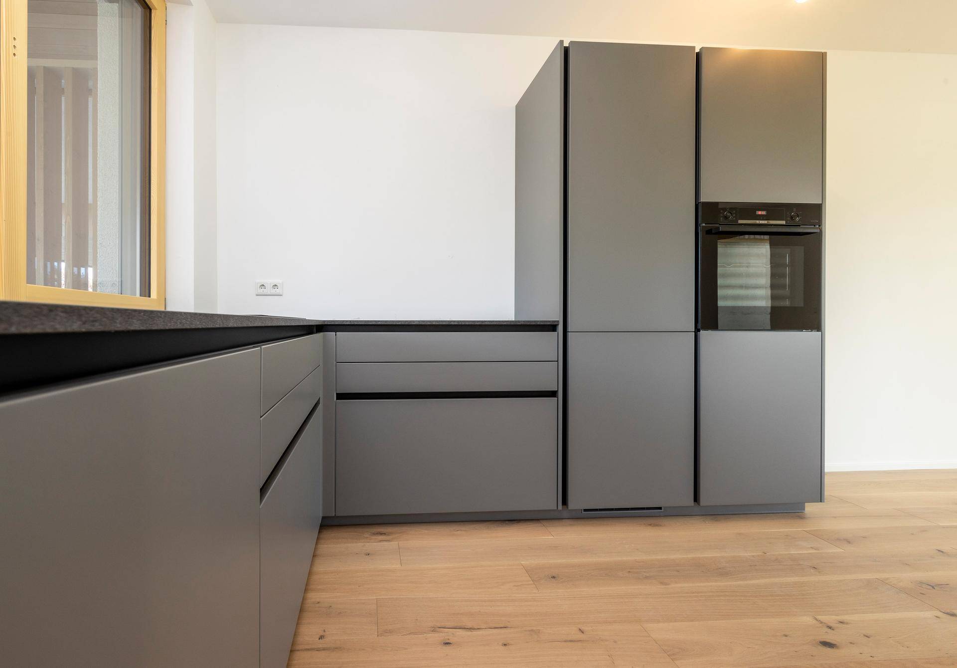 Integrierte Küchengeräte wie Backofen und Kühlschrank in grauen Schränken.