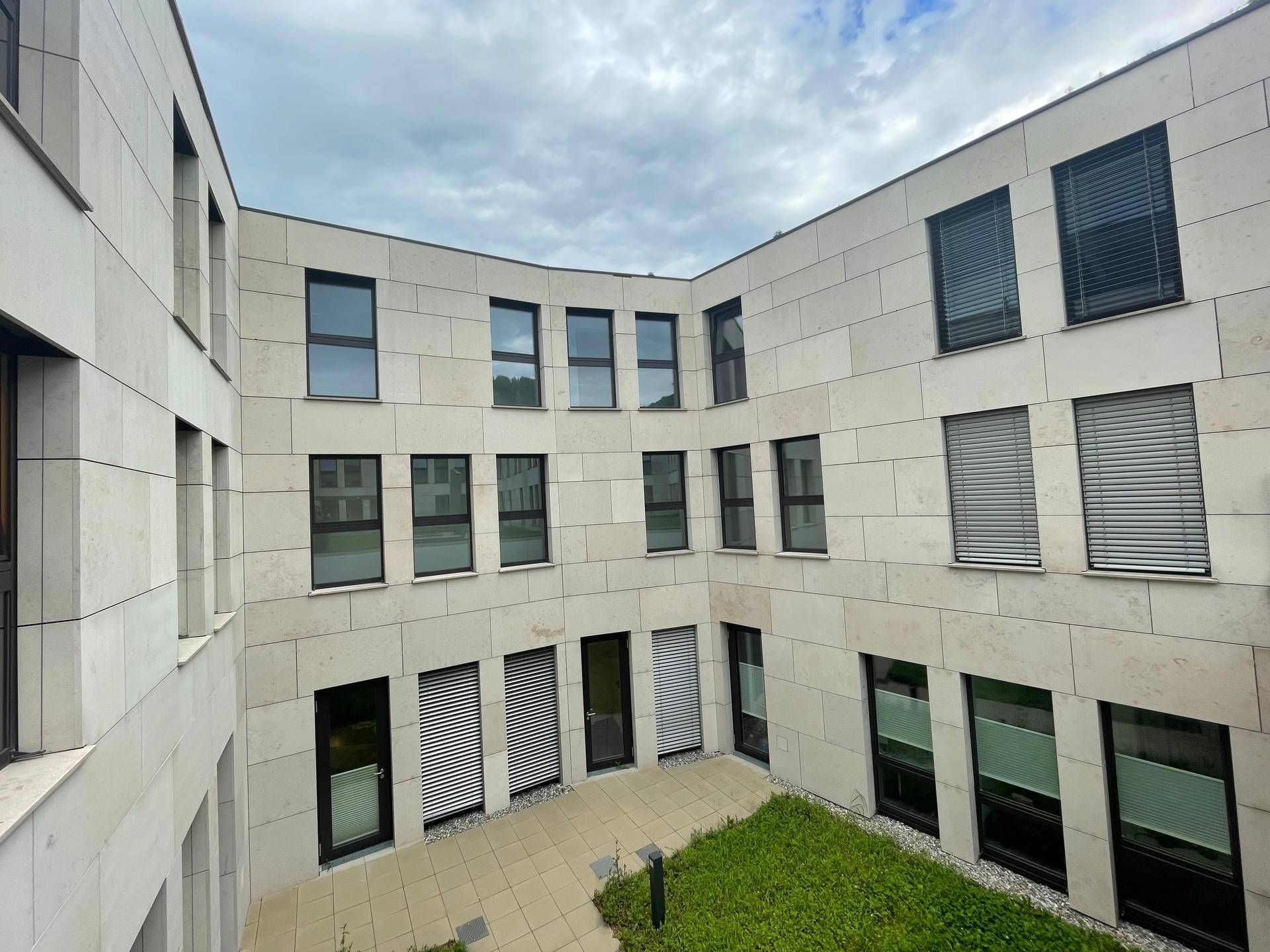 Innenhof eines modernen Gebäudes mit hellen Fassaden, vielen Fenstern und einer kleinen Grünfläche.