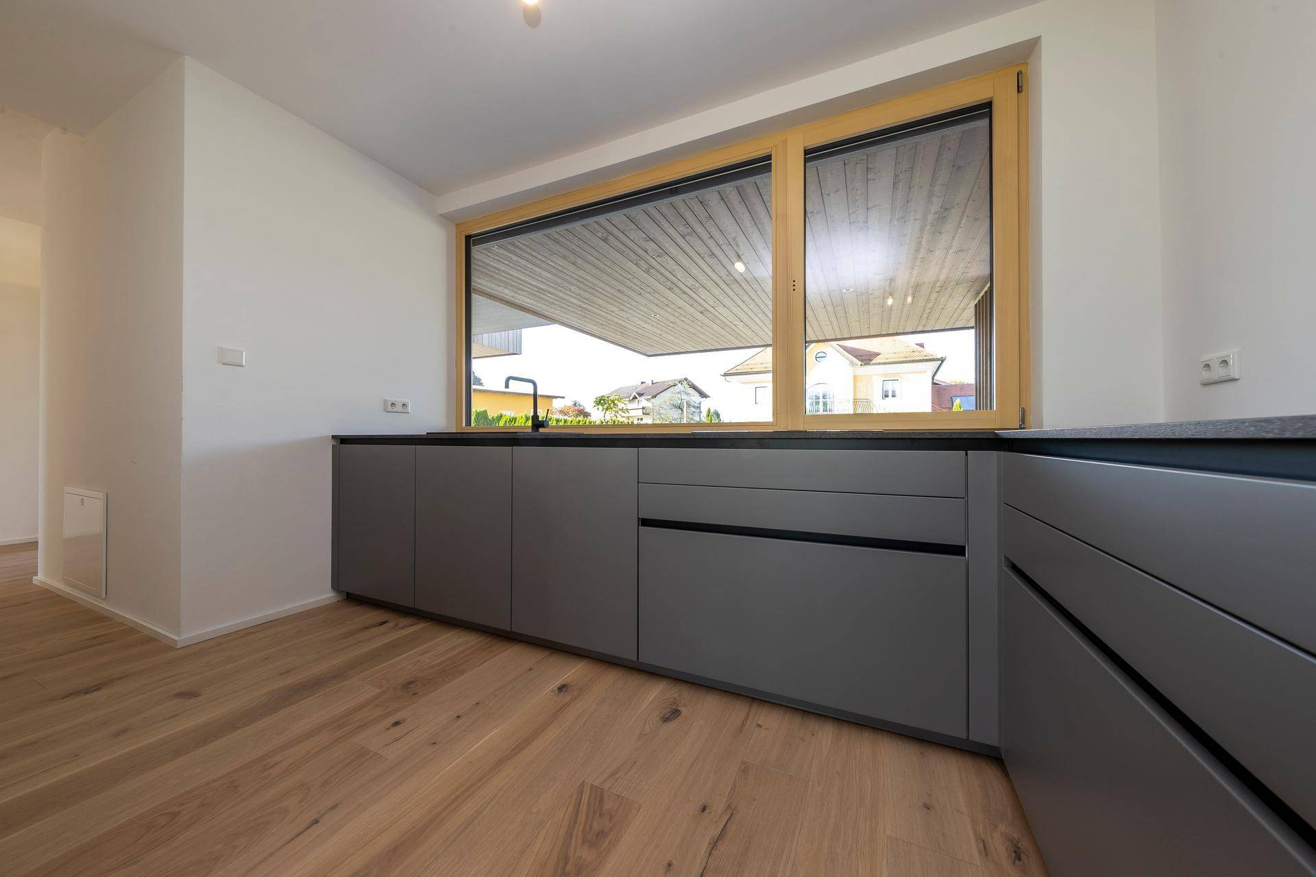 Moderne Einbauküche mit grauen Fronten, dunkler Arbeitsplatte und Fenster.